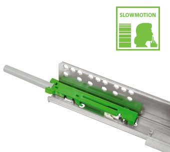 Imagem de um dispositivo mecânico verde e prateado, possivelmente uma corrediça de gaveta ou mecanismo de fechamento suave. O canto superior direito apresenta o ícone de uma silhueta com um dedo nos lábios e a palavra “SLOWMOTION” acima das linhas horizontais. Este sofisticado sistema de corrediças garante um funcionamento suave e silencioso.