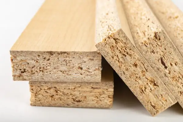 Imagem aproximada de quatro pedaços de painéis de partículas mostrando suas seções transversais e texturas de superfície. As placas, incluindo as variantes de MDF e MDP, possuem revestimento de folheado de madeira leve na superfície, enquanto o interior é composto por lascas e partículas de madeira compactada.